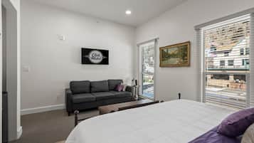 Un dormitorio con cama, sofá, un cuadro y ventana con persianas.