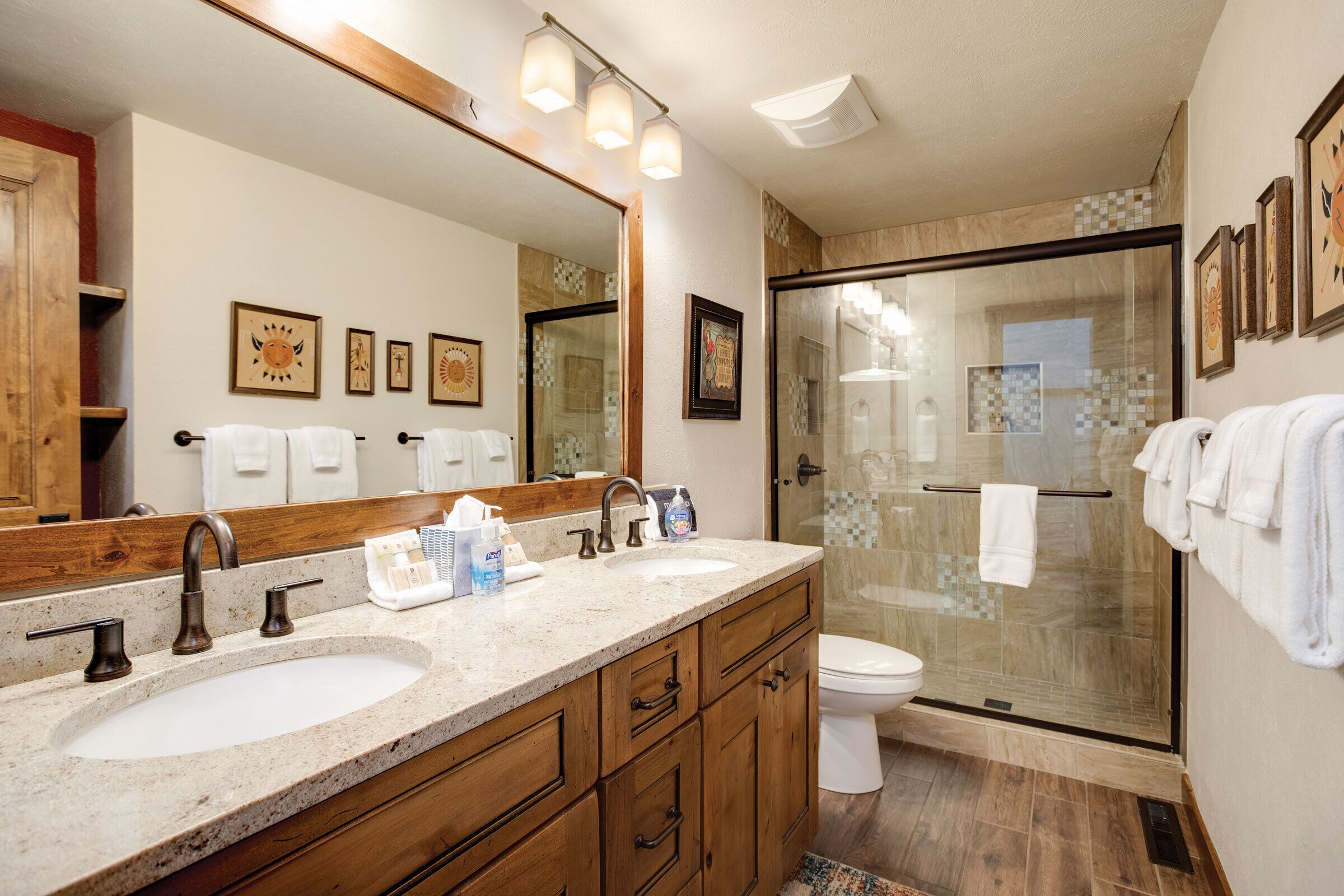 A bathroom with two sinks, a toilet, a glass shower enclosure, and wooden cabinets.