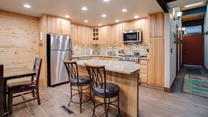Una cocina con armarios de madera, un refrigerador de acero inoxidable, un microondas y una isla grande con taburetes de bar.