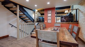 Un comedor con una mesa y sillas de madera, una escalera con barandilla y una pared decorada con cuadros.