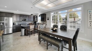 A modern kitchen with dark cabinetry, stainless steel appliances, and a large dining table with cushioned benches.