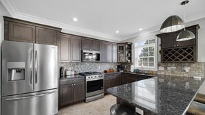 A modern kitchen with stainless steel appliances, dark wood cabinets, a granite countertop, and pendant lighting.