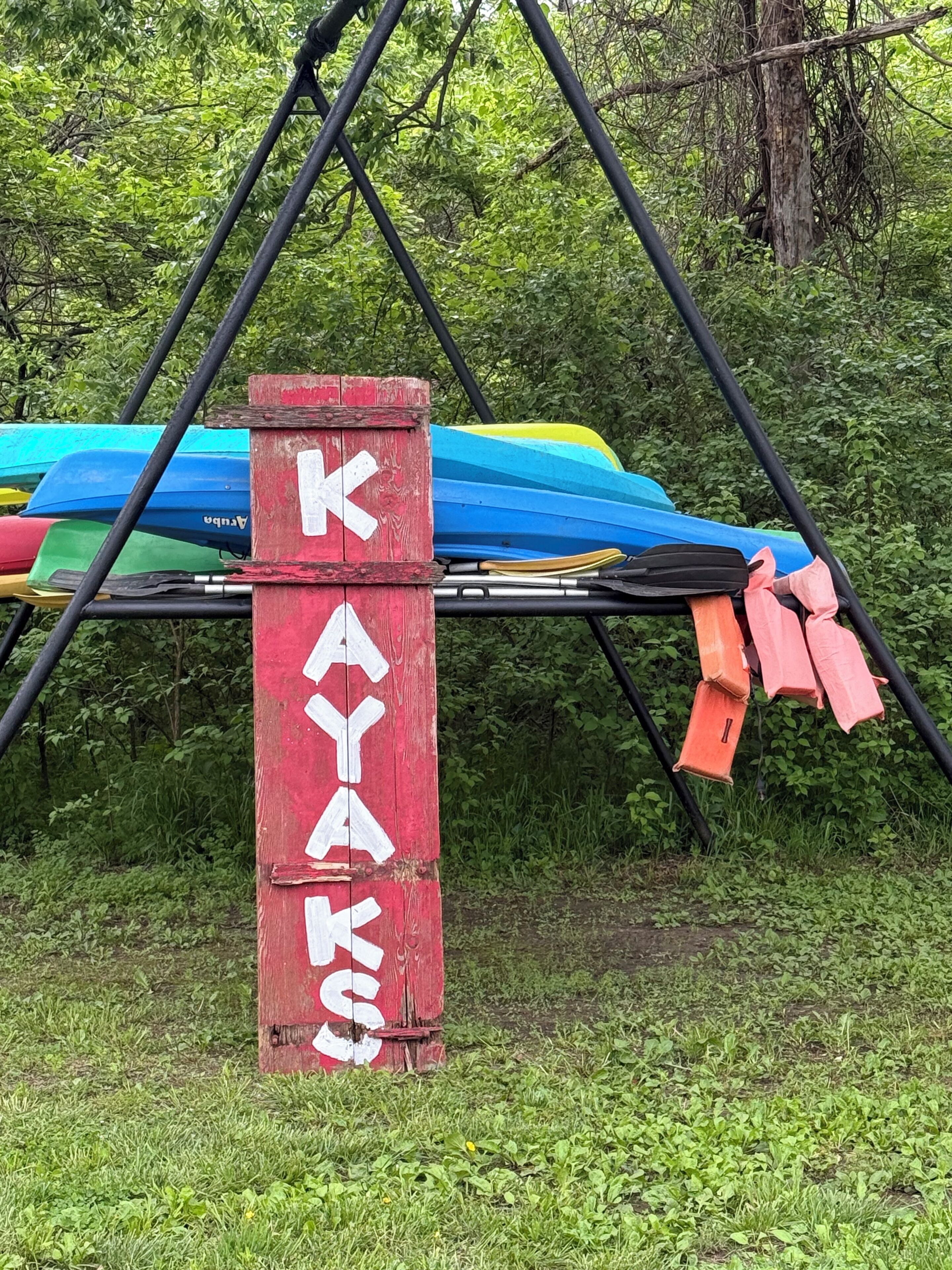 Un segnale rosso con lettere bianche che indicano 'KAYAKS' e un portKayak con kayak colorati.