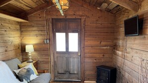 L’intérieur d’un chalet accueillant, avec une porte en bois, un canapé, une lampe, un téléviseur et un petit radiateur.