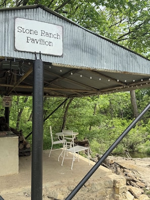 A Stone Ranch Pavilion with a metal roof, a table and chairs, and a sign indicating the name. - Buffalo Cabin - Private Pond, Kayaks, Fire Pit on 150 Acres (Gridley)