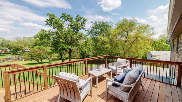 Une terrasse en bois avec des meubles d’extérieur, une vue sur un parc et une maison en arrière-plan.