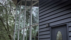 Une maison à l’extérieur sombre, dotée d’un grand porche vitré et d’une porte d’entrée sombre agrémentée d’un panneau de verre décoratif.