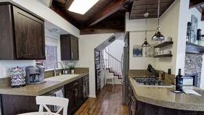 Une cuisine moderne avec des meubles en bois foncé, un plan de travail en granit, une cuisinière encastrée et un coin repas agrémenté d’une chaise blanche.