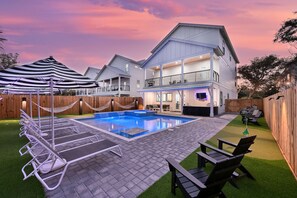 A two-story house with a swimming pool, lounge chairs, and a covered patio area.