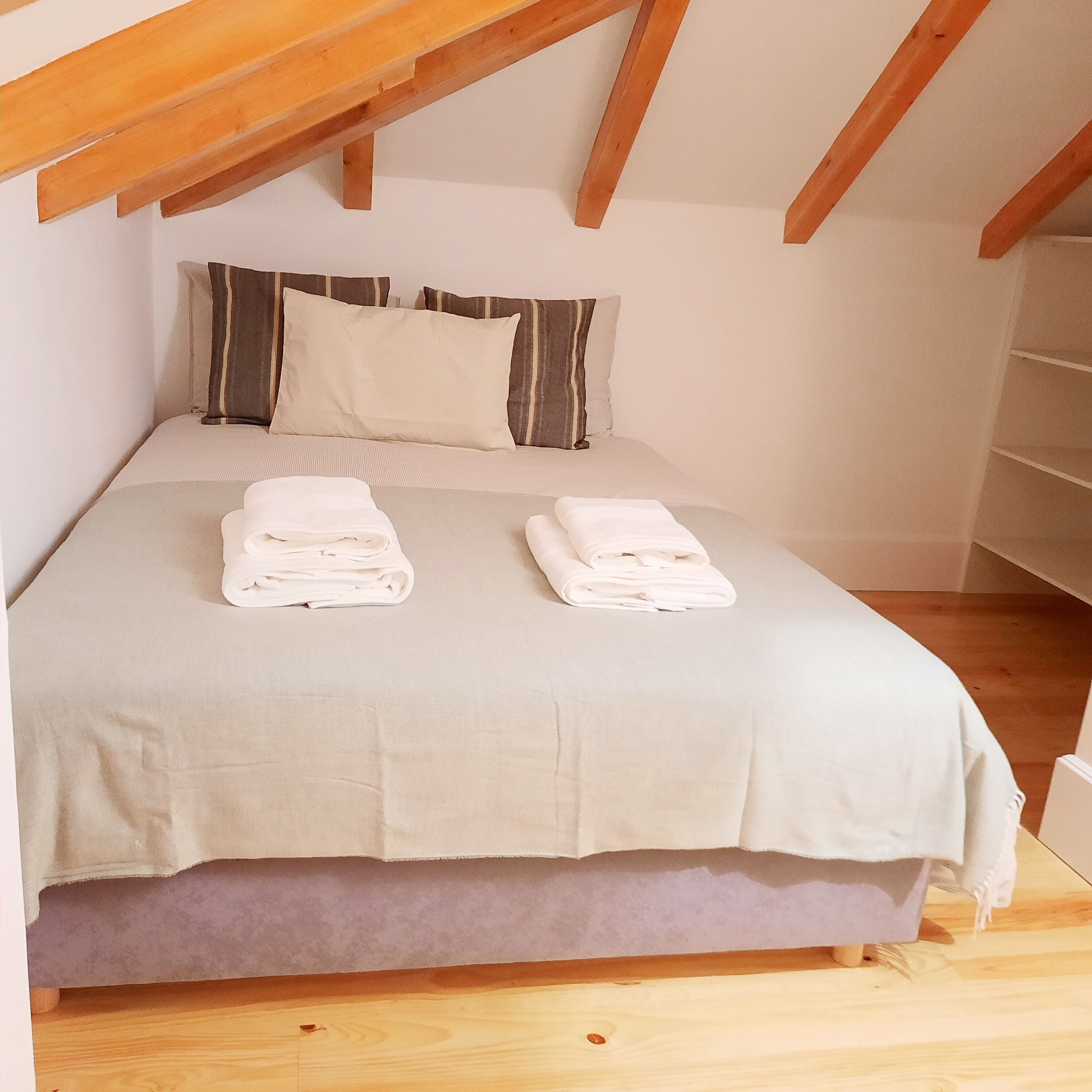 A neatly made bed with two folded towels, a striped pillow, and a plain pillow on a light-colored bedspread.