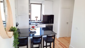 Et moderne køkken med hvide skabe, en sort bordplade og en central ø med barstole.