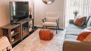 Ein Wohnzimmer mit Fernseher, einem runden Spiegel, einem Sessel, einer Couch und einem dekorativen Kürbis.