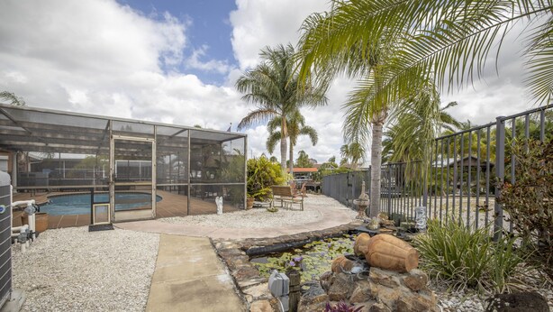 A backyard with a pool, a covered seating area, and a small pond with rocks and plants.