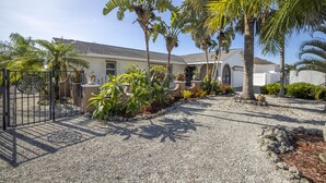 A house with a gravel driveway, palm trees, and a gated entrance.