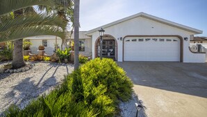 A single-story house with a garage, surrounded by a gravel driveway and lush greenery.