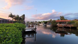 A marina with boats docked, a covered area with chairs, and lush greenery along the water's edge.