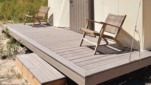 A tented accommodation with a wooden deck, two wicker chairs, and a door. - Firepit-Shade-Chairs-Dark Skies (Levan)