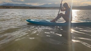 A person sitting on a paddleboard in calm water with mountains in the background. - Firepit-Shade-Chairs-Dark Skies (Levan)