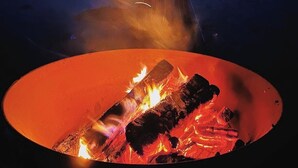 A campfire in a circular fire pit with a mountainous landscape in the background under a night sky. - Firepit-Shade-Chairs-Dark Skies (Levan)