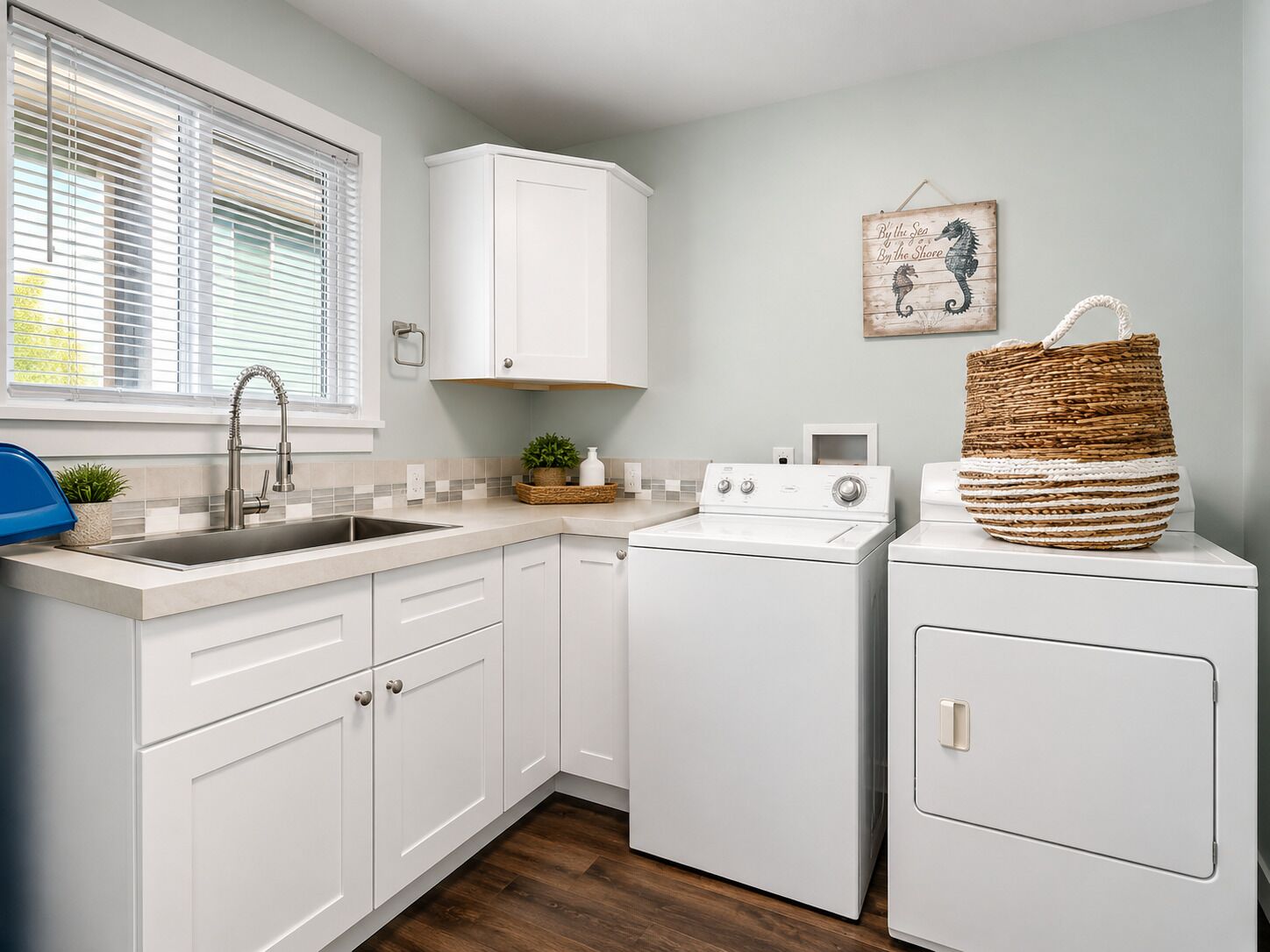 A kitchen with white cabinets, a sink, a washing machine, and a decorative seahorse wall art piece.
