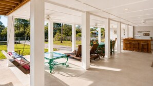Un espace extérieur abrité comprenant une balançoire, une table en verre, des chaises, un coin bar et une vue sur un parc.