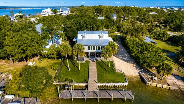 Une grande maison avec un quai et une pelouse, entourée d’arbres et bordée par l’eau.