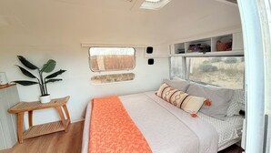 Een slaapkamer met een bed, een raam, een plank met boeken en een plant.