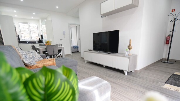 A modern living room with a grey sofa, a flat-screen TV, and a white entertainment unit. - Casas do Baleeiro - Whaler’s Houses (Machico)
