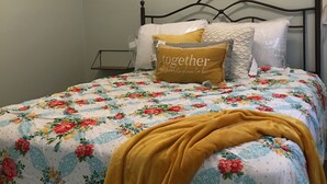 A bed with a floral bedspread, a mustard-colored throw blanket, and a decorative wall hanging. - The Cranny @ Cookson —Tiny House Experience!!  Night,  week & monthly stays (Cookson)