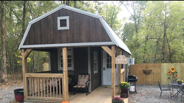 A rustic wooden cabin with a porch, a chair, and a sign that reads "The Porch Not a Motel." - The Cranny @ Cookson —Tiny House Experience!!  Night,  week & monthly stays (Cookson)