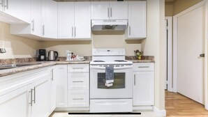 A kitchen with white cabinets, a stove, and a coffee maker. - Private Rooms Downtown River Valley Condo Men only Non Smoking. (Edmonton)