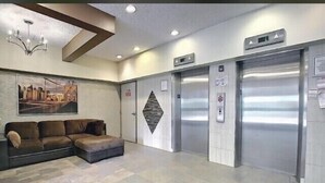 A lobby with a sectional sofa, two elevators, a chandelier, and a cityscape painting on the wall. - Private Rooms Downtown River Valley Condo Men only Non Smoking. (Edmonton)