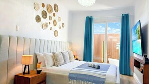 Una habitación de hotel con una cama grande, televisión y balcón con cortinas.