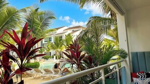 Un balcón con vista a un área de piscina, rodeado de palmeras y sillas de descanso.