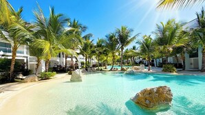 Un área de piscina en un resort con agua turquesa cristalina, palmeras y rocas grandes.