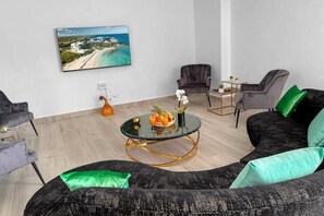 A modern living room with a black sofa, two armchairs, a glass coffee table with fruit, and a painting of a beach scene. - Beach Villa Fiesta with Pool, BBQ and Maid incl. (Punta Cana)