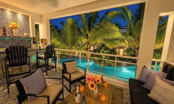 Un balcón con vista a la piscina, mobiliario de mimbre y decoración tropical.