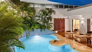 Ein Innenpool mit geschwungenem Design, umgeben von üppiger tropischer Vegetation und ausgestattet mit Liegestühlen sowie einer kleinen Insel mit Wasserspiel.