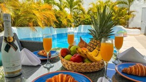 Colazione con croissant, frutta, succo e champagne accanto a una piscina.