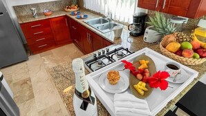 Una cucina con piani di lavoro in granito, mobili rossi, un piano cottura a gas, una macchina per caffè e un cesto di frutta.