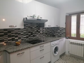 A compact kitchen with white cabinets, a black and white tiled backsplash, a granite countertop, a built-in washing machine, and a window with curtains. - Apartment in a rural house with a large garden 5 minutes from the beach (sales, colunga)