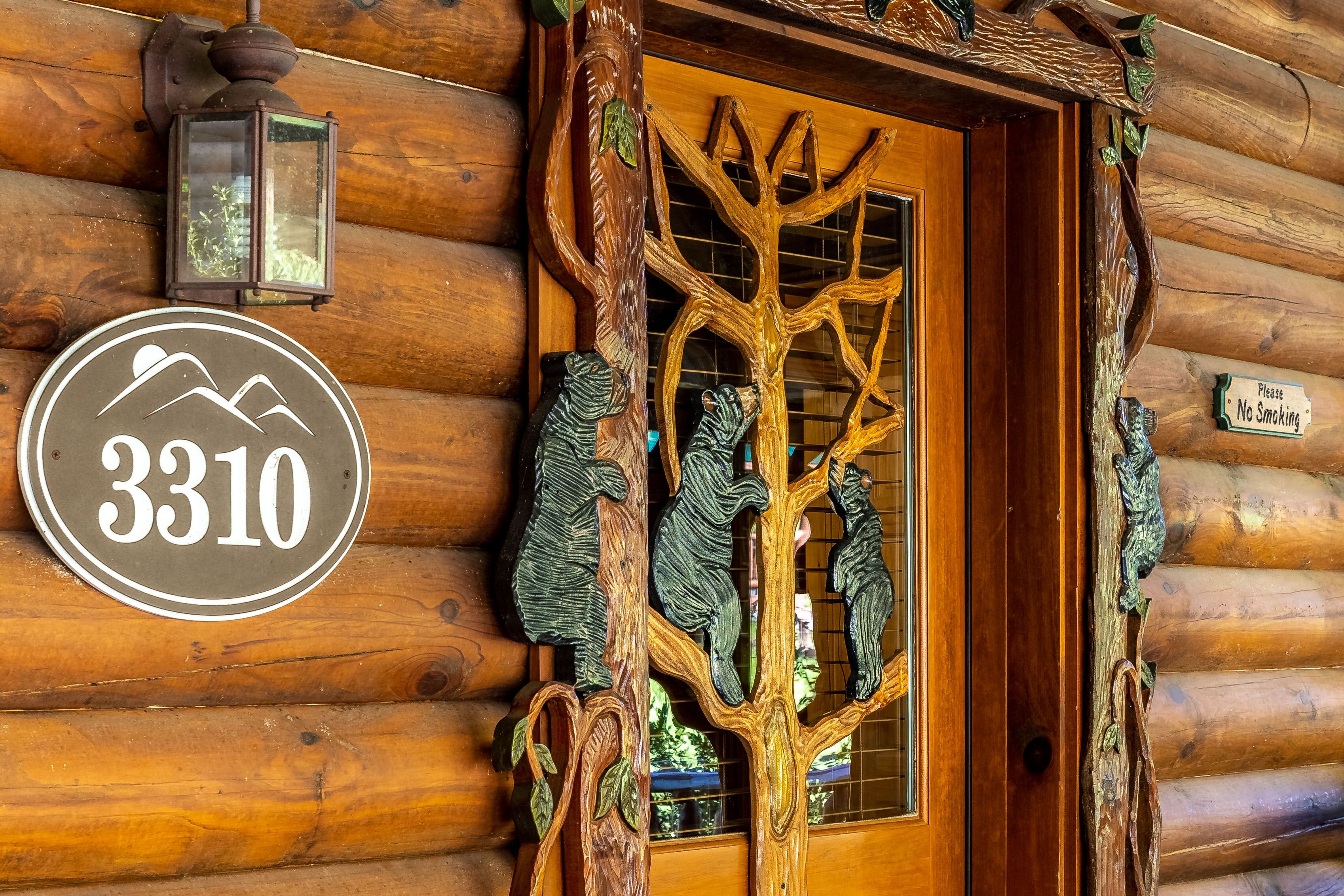 Une cabane en rondins de bois avec une porte sculptée en forme d’arbre, une pancarte indiquant « 3310 » et une autre interdisant de fumer.