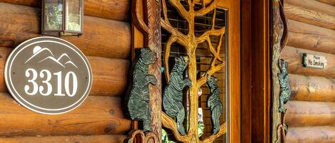 Une cabane en rondins de bois avec une porte sculptée en forme d’arbre, une pancarte indiquant « 3310 » et une autre interdisant de fumer.