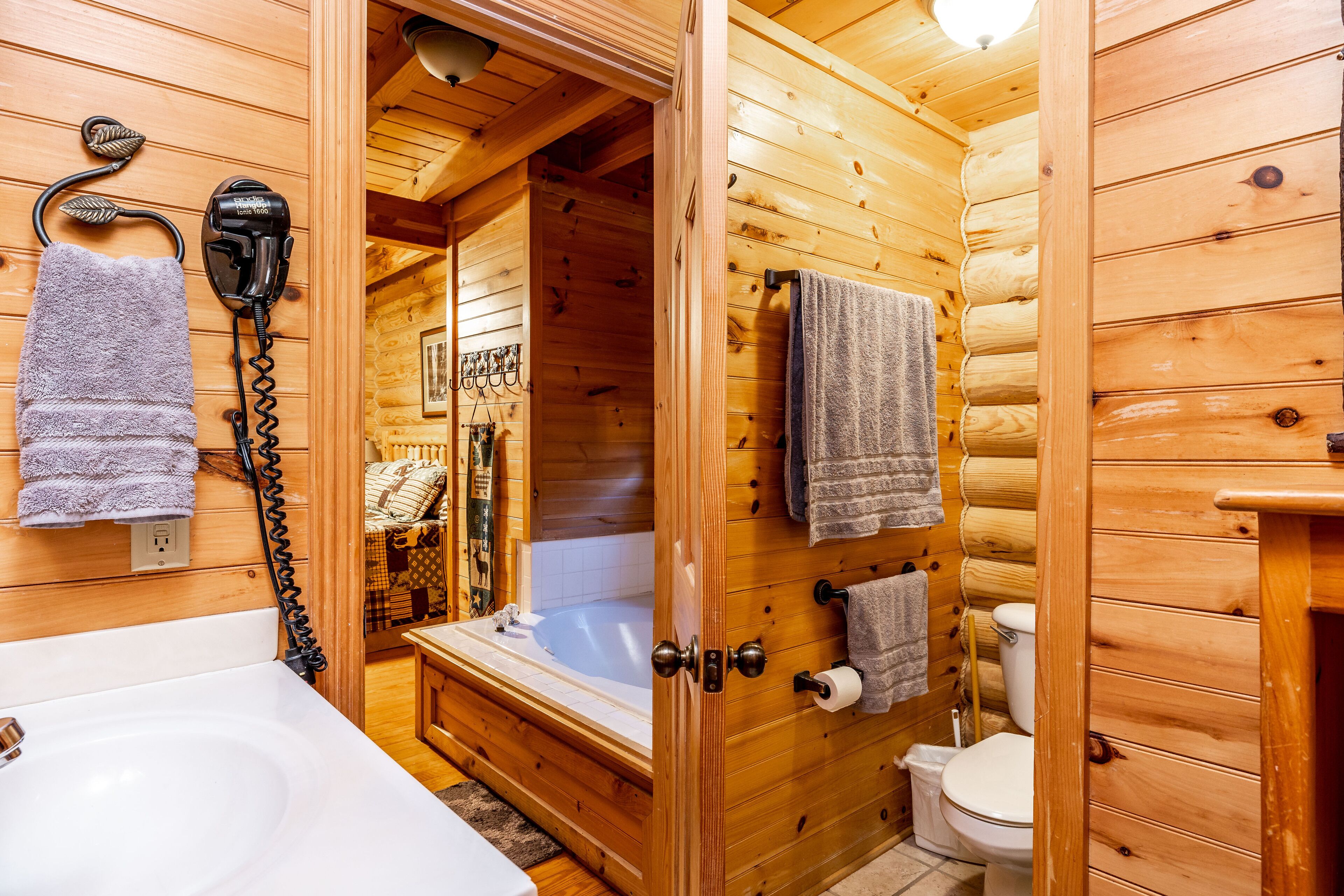 A wooden cabin bathroom with a bathtub, toilet, and a hairdryer on the wall.