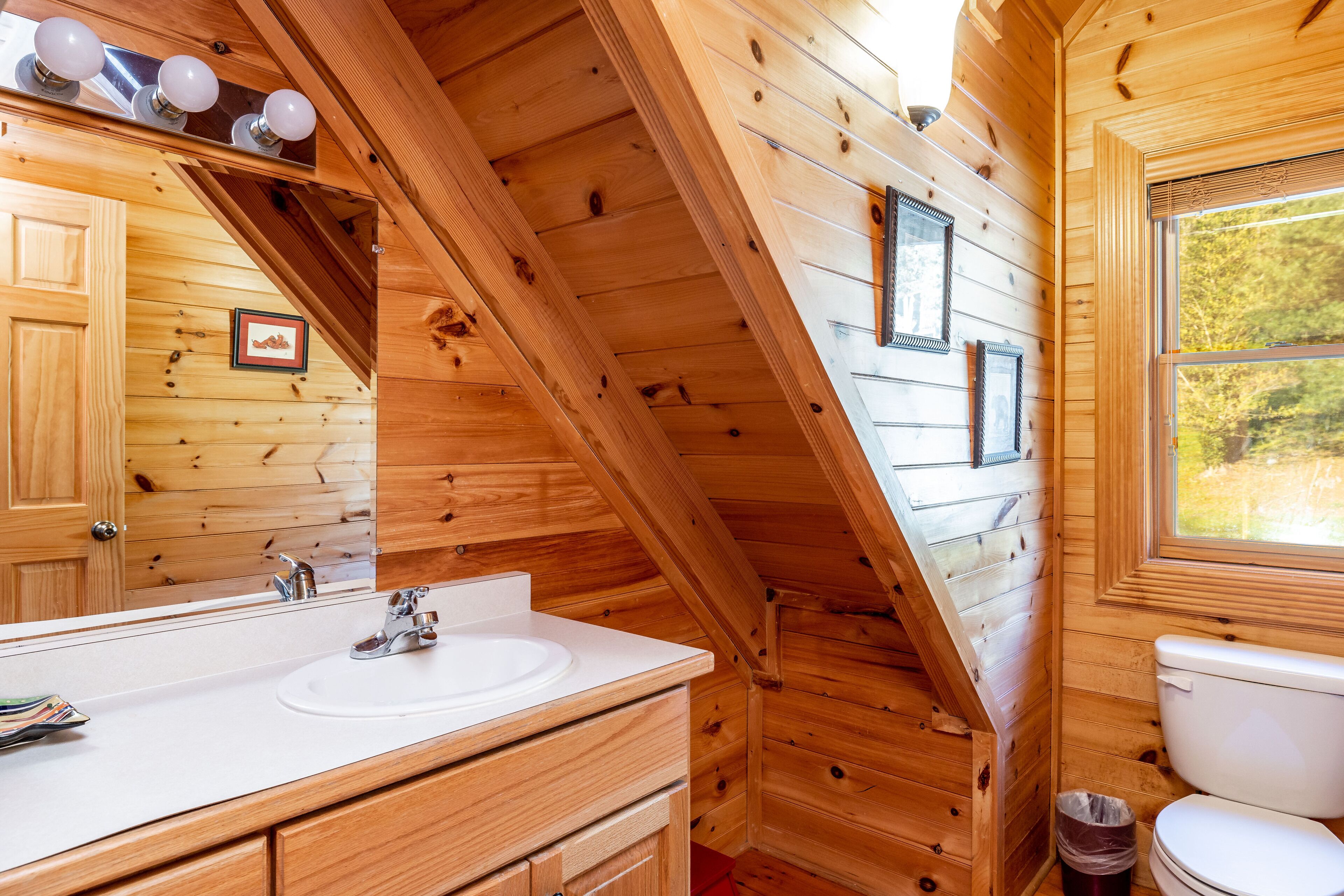 A wooden cabin bathroom with a white sink, mirror, and toilet.