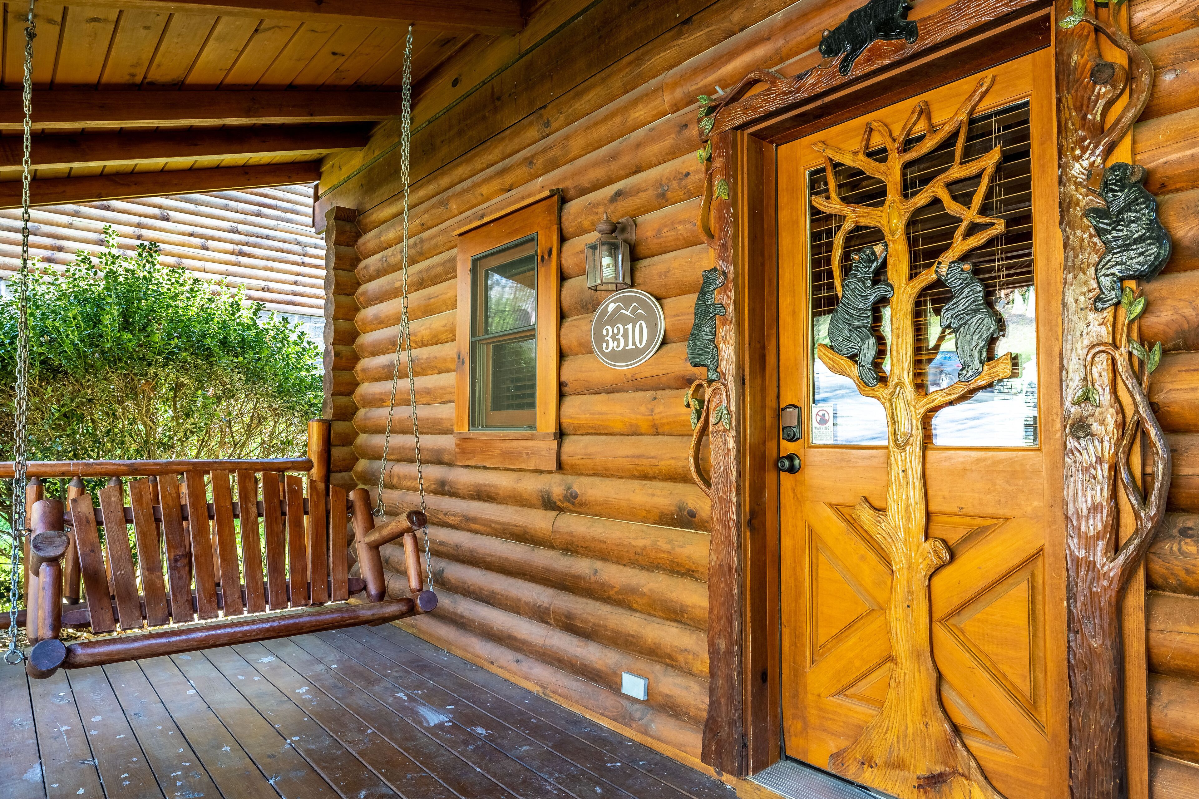Een houten vakantiehuisje met een veranda, een deur met een houtsnede van een boom en een brievenbus met het nummer 3310.