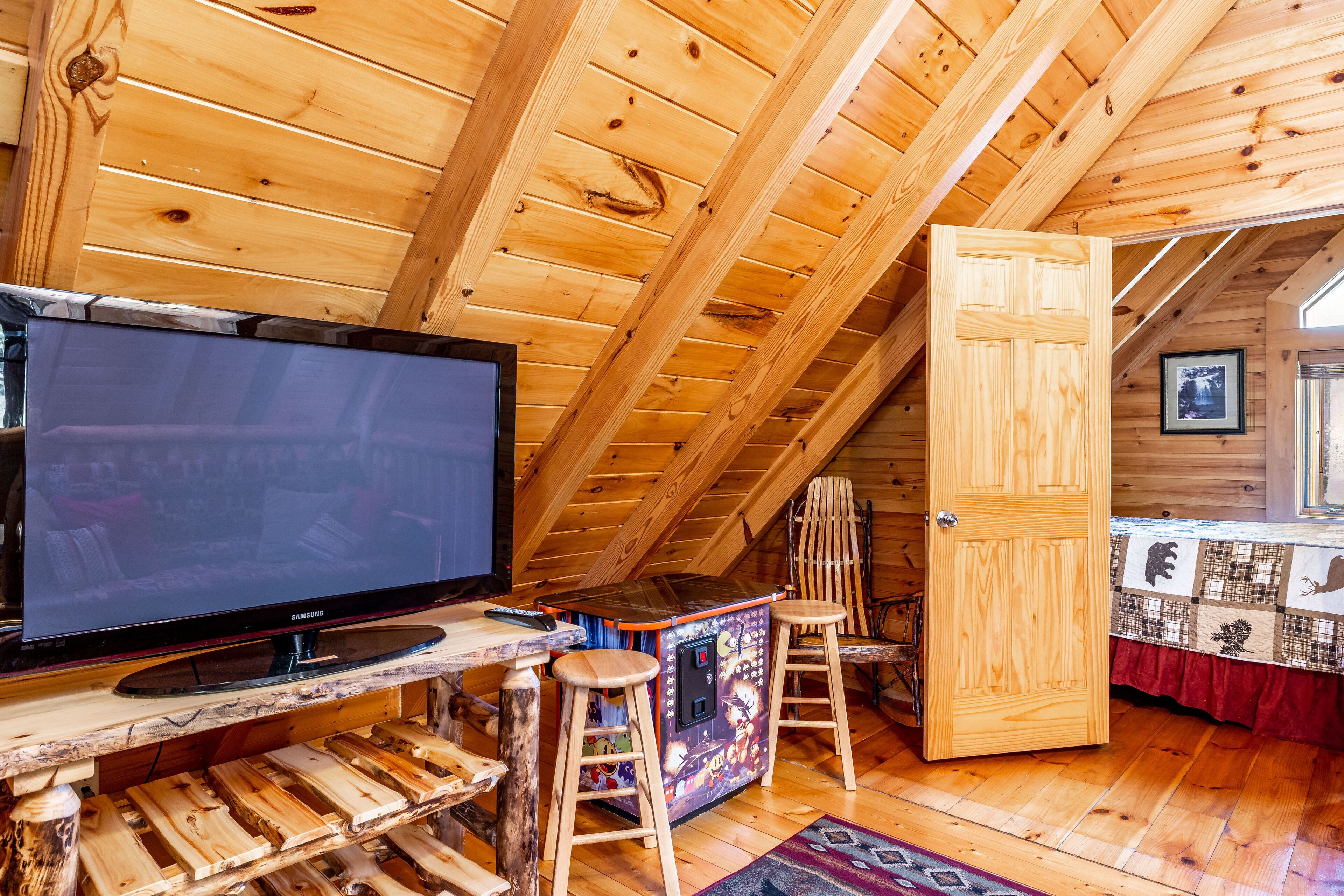 A cozy room with a large TV, wooden furniture, and a high ceiling.