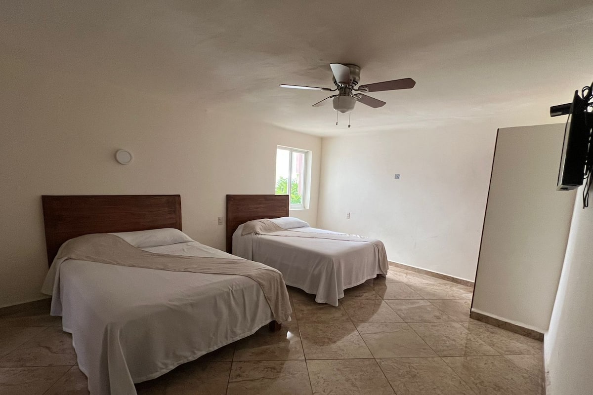 Una habitación con dos camas, ventilador de techo, ventana y puerta.
