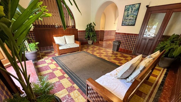 A spacious lobby with a checkered floor, a wooden sofa, a bed, and several potted plants. - Hotel Catedral Cuernavaca (Cuernavaca)