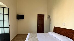 A bedroom with a bed, a television on the wall, a door, and a tiled floor. - Hotel Catedral Cuernavaca (Cuernavaca)